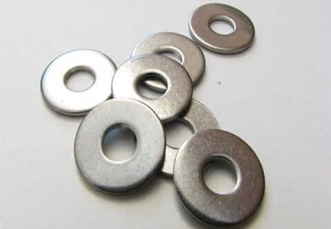 A close-up view of six metallic flat washers arranged on a white surface